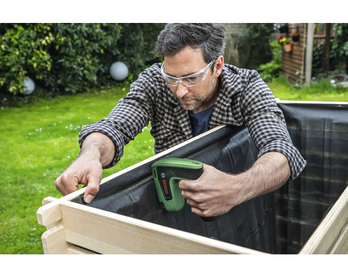 Ein Handwerker nutzt einen Bosch Tacker zum Befestigen der Innenfolie an einem hölzernen Hochbeet im Garten.