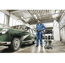 Un homme nettoie une voiture ancienne avec un nettoyeur haute pression Karcher dans un atelier.