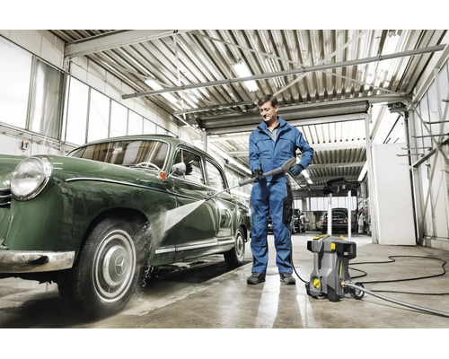 Un homme nettoie une voiture ancienne avec un nettoyeur haute pression Karcher dans un atelier.