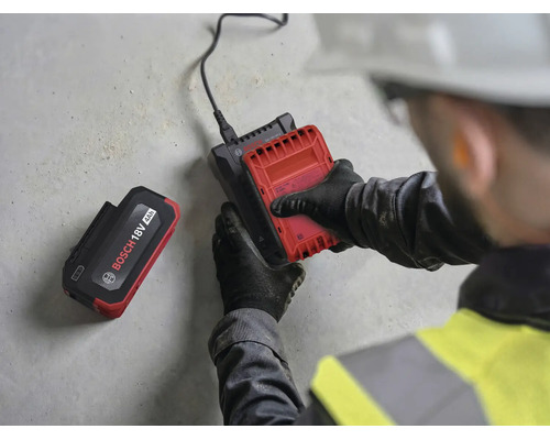 Handwerker legt einen 18 Volt Akku in ein Bosch Ladegerät ein, ein weiterer 4 Amperestunden Akku liegt daneben.