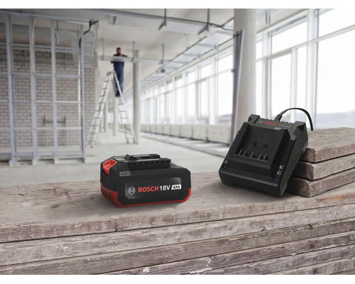 Bosch Akku und Ladegerät 18 Volt auf einer Holzstapel Unterlage vor einer Baustelle mit arbeitender Person auf einer Leiter.