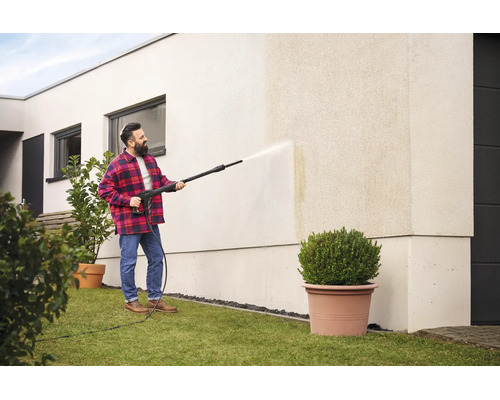 Un homme nettoie le mur extérieur d une maison moderne avec un nettoyeur haute pression.