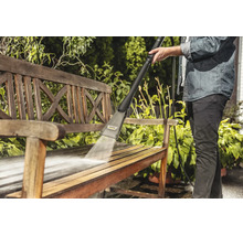 Une personne nettoie un banc de jardin en bois avec un nettoyeur haute pression Karcher en extérieur.