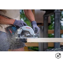 Eine Person benutzt eine akkubetriebene Bosch Handkreissäge mit einem ProCORE 18 Volt Akku, um einen Holzbalken auf einer Baustelle zu sägen. (Image AI modified or generated)