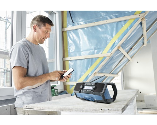 Un homme utilise un téléphone portable à côté d'une radio de chantier dans une pièce aux murs inachevés.