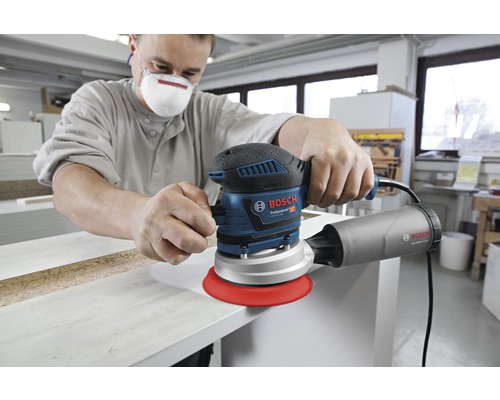 Un homme ponce une planche de bois avec une ponceuse excentrique Bosch
