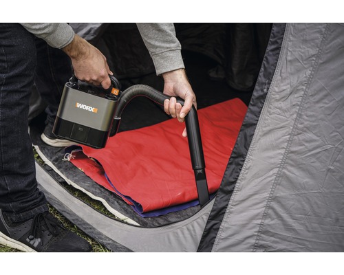 Une personne utilise un aspirateur sans fil WORX dans une tente.