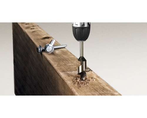 Une perceuse perce un trou dans une planche de bois, des vis sont à côté.