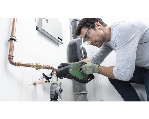 Un artisan utilise une scie sabre Bosch pour couper un tuyau en cuivre. Il porte des équipements de protection, notamment des lunettes de sécurité et des gants.