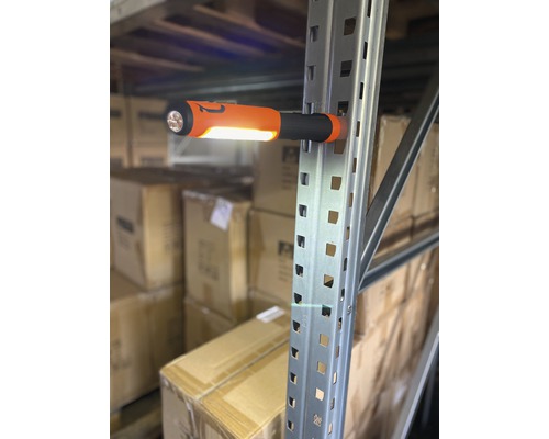 Une lampe de travail orange est fixée magnétiquement sur une étagère métallique.