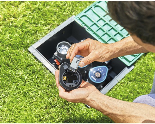 Un homme insère une pile dans un ordinateur d''irrigation situé dans un puits dans la pelouse