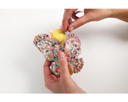 Mains façonnant un papillon décoratif avec des paillettes