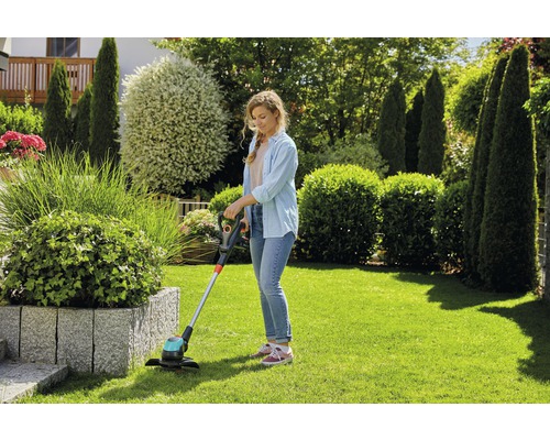 Frau schneidet Rasen mit einem Rasentrimmer im Garten.