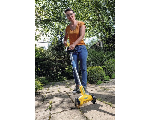 Une femme utilise un désherbeur de joints pour enlever les mauvaises herbes sur un trottoir.