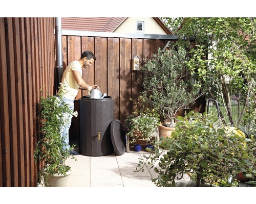 Scène de jardin avec réservoir d''eau de pluie, homme avec arrosoir et clôture en bois