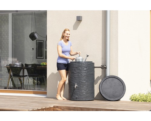 Frau befüllt Giesskanne an Regentonne im Garten