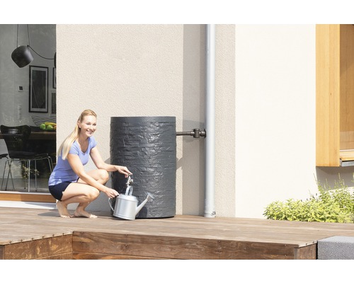 Frau befüllt Giesskanne an einer grauen Regentonne im Garten