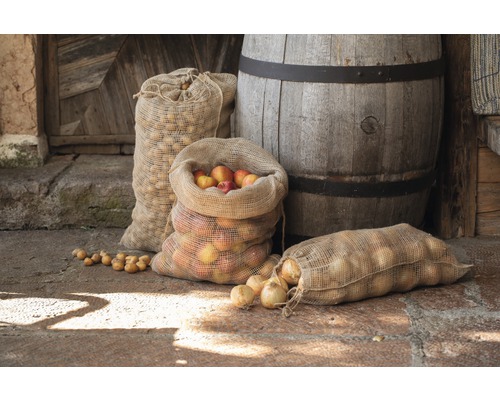 Sacs de jute remplis de pommes, d''oignons et de pommes de terre devant un fût en bois