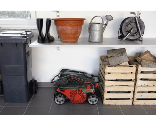 Local de stockage avec poubelle, bottes en caoutchouc, pot de fleurs, arrosoir, enrouleur de câble, tondeuse à gazon et caisses en bois