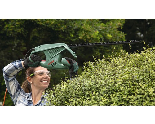 Eine Frau schneidet mit einer elektrischen Heckenschere von Bosch eine Hecke.