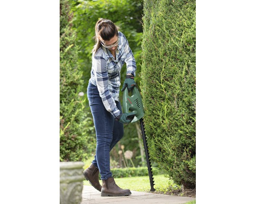 Frau schneidet Hecke mit Heckenschere im Garten.