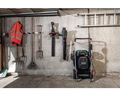 Outils de jardin, souffleurs de feuilles, tondeuse à gazon et échelle sur un mur dans un garage.