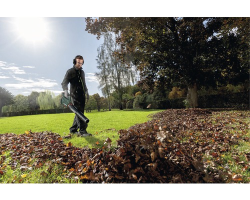 Un homme utilise un souffleur de feuilles dans le jardin pour enlever les feuilles.