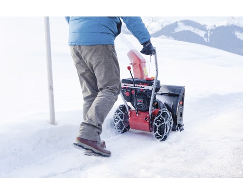 Une personne pousse une fraise à neige sur une surface enneigée.