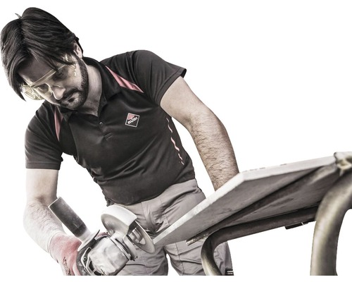 Un artisan coupe un carreau avec une meuleuse sur une table de travail. Il porte des lunettes de protection et des gants. Logo Rubi.