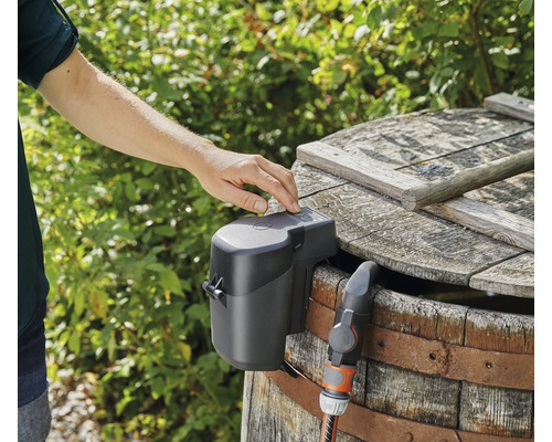 Distributeur d''eau automatique sur un réservoir d''eau de pluie avec raccord de tuyau et manipulation par une main.