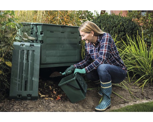 Une femme remplit un composteur de jardin avec un seau et une pelle.
