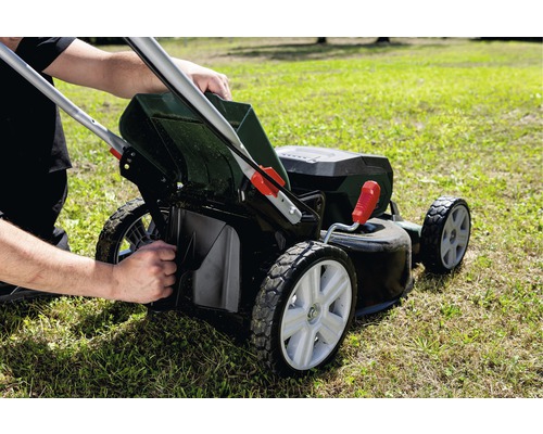 Une personne vide le bac de ramassage d''une tondeuse à gazon sur une pelouse.