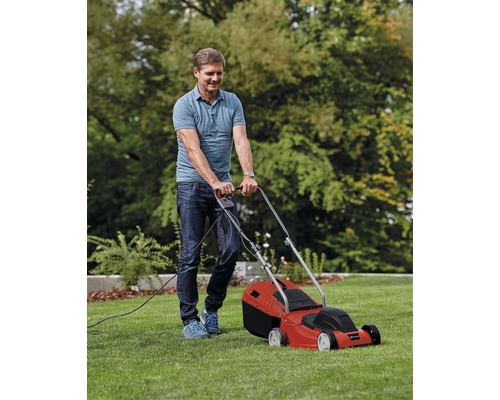 Un homme tond la pelouse avec une tondeuse à gazon électrique rouge dans le jardin.