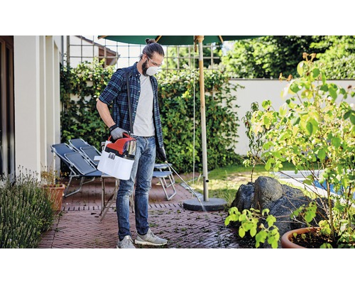 Homme avec masque de protection et pulvérisateur de jardin pour désherber une terrasse