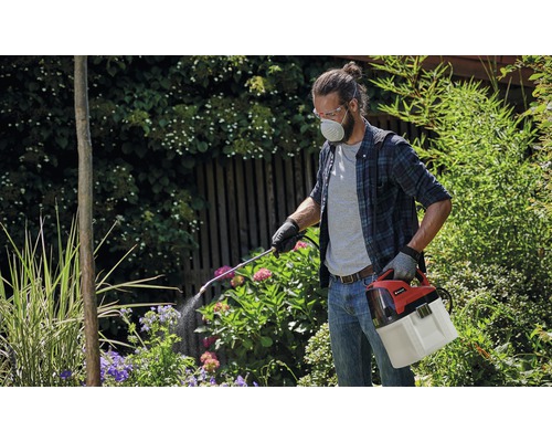 Homme portant des lunettes de protection et un masque respiratoire utilisant un pulvérisateur de plantes à batterie dans le jardin.