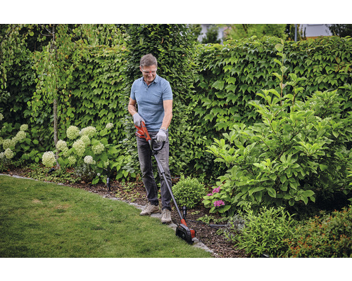 Un homme coupe les bordures de pelouse avec un coupe-bordures dans le jardin.