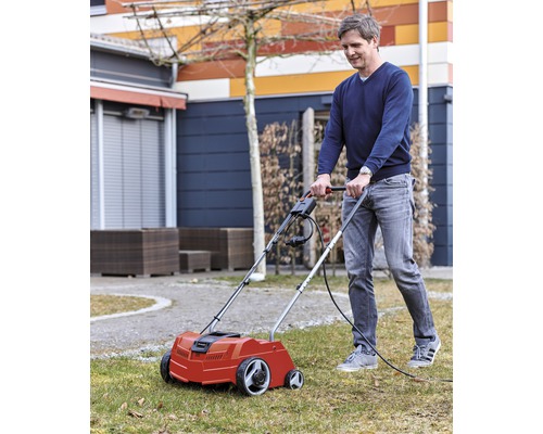 Un homme utilise un scarificateur électrique dans le jardin pour entretenir la pelouse.