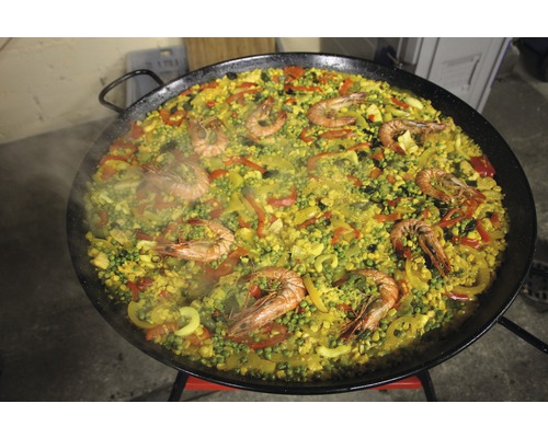 Paella mit Meeresfrüchten, Reis und Gemüse in großer Pfanne.