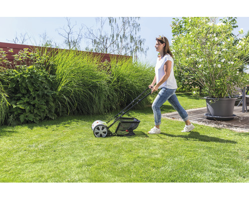 Eine Frau benutzt einen Rasenlüfter im Garten, um den Rasen zu pflegen.
