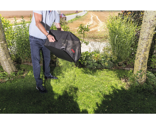 Une personne vide un sac à feuilles sur une pelouse dans le jardin.
