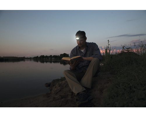 Homme assis à l''extérieur lisant un livre avec une lampe frontale