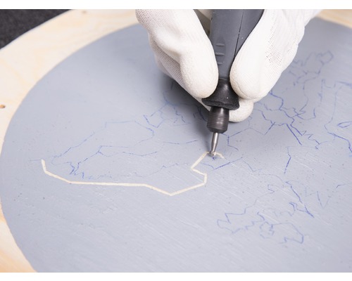 Une main gantée utilise un outil multifonction sur un cercle en bois peint.