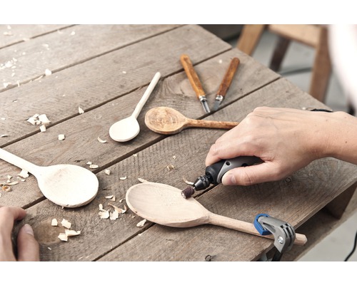 Scène artisanale avec des cuillères en bois, des outils de sculpture et un outil rotatif sur une surface en bois