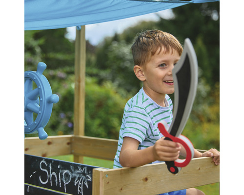 Garçon jouant avec un bateau jouet et une épée jouet dans le jardin