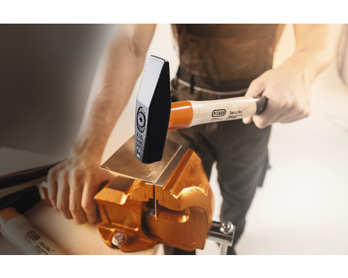 Ein Mann bearbeitet ein Metallstück mit einem Hammer und Schraubstock von Picard.