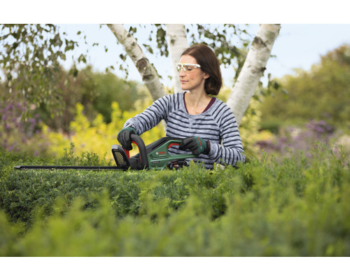 Femme taillant une haie avec un taille-haie sans fil dans le jardin