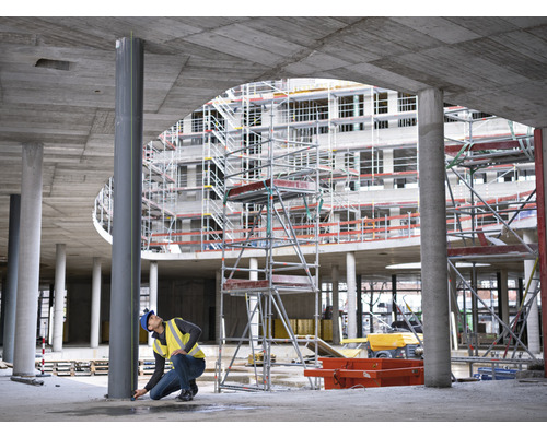 Bauarbeiter misst eine Stahlsäule auf einer Baustelle.