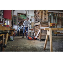 Ein Mann benutzt einen Rasenlüfter in einer Werkstatt voller Holz und Werkzeuge.