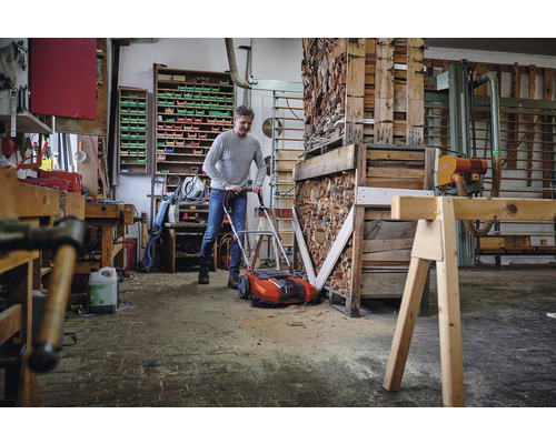 Un homme utilise un scarificateur dans un atelier rempli de bois et d''outils.