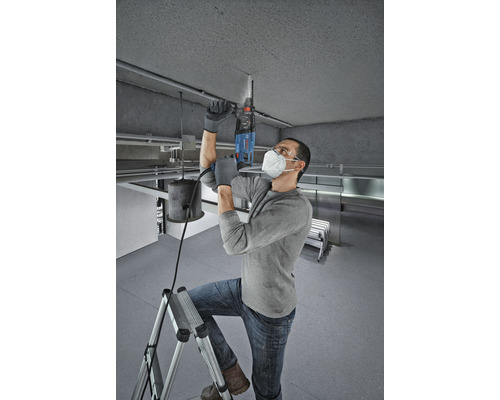 Un homme perce le plafond avec un marteau perforateur debout sur une échelle